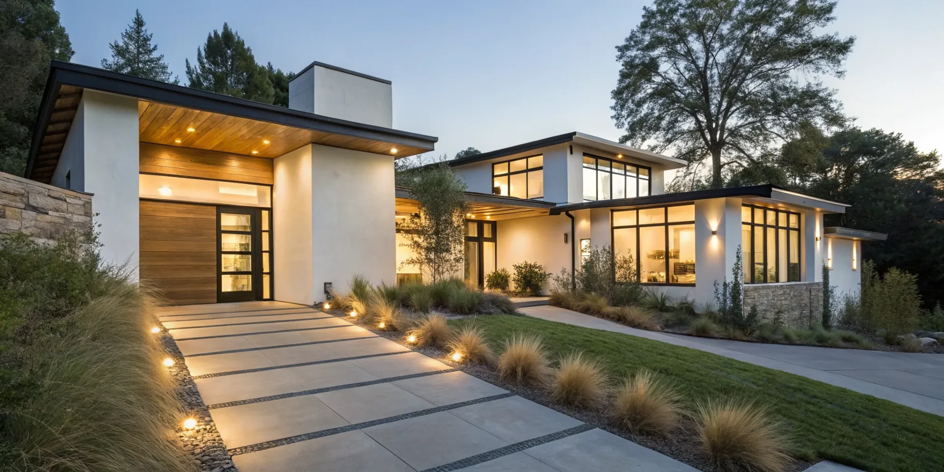 Custom outdoor lighting illuminates the walkway and landscaping of a modern home at dusk.